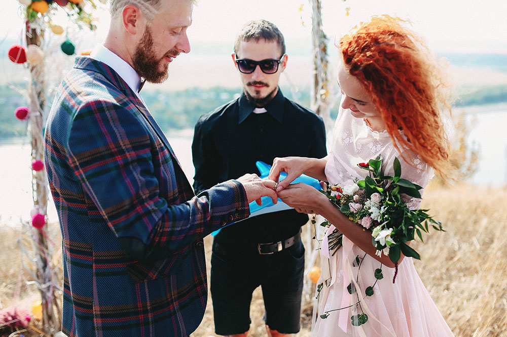 A happy couple get married by a wedding officiant outdoors and exchanges rings in a sunny wedding ceremony